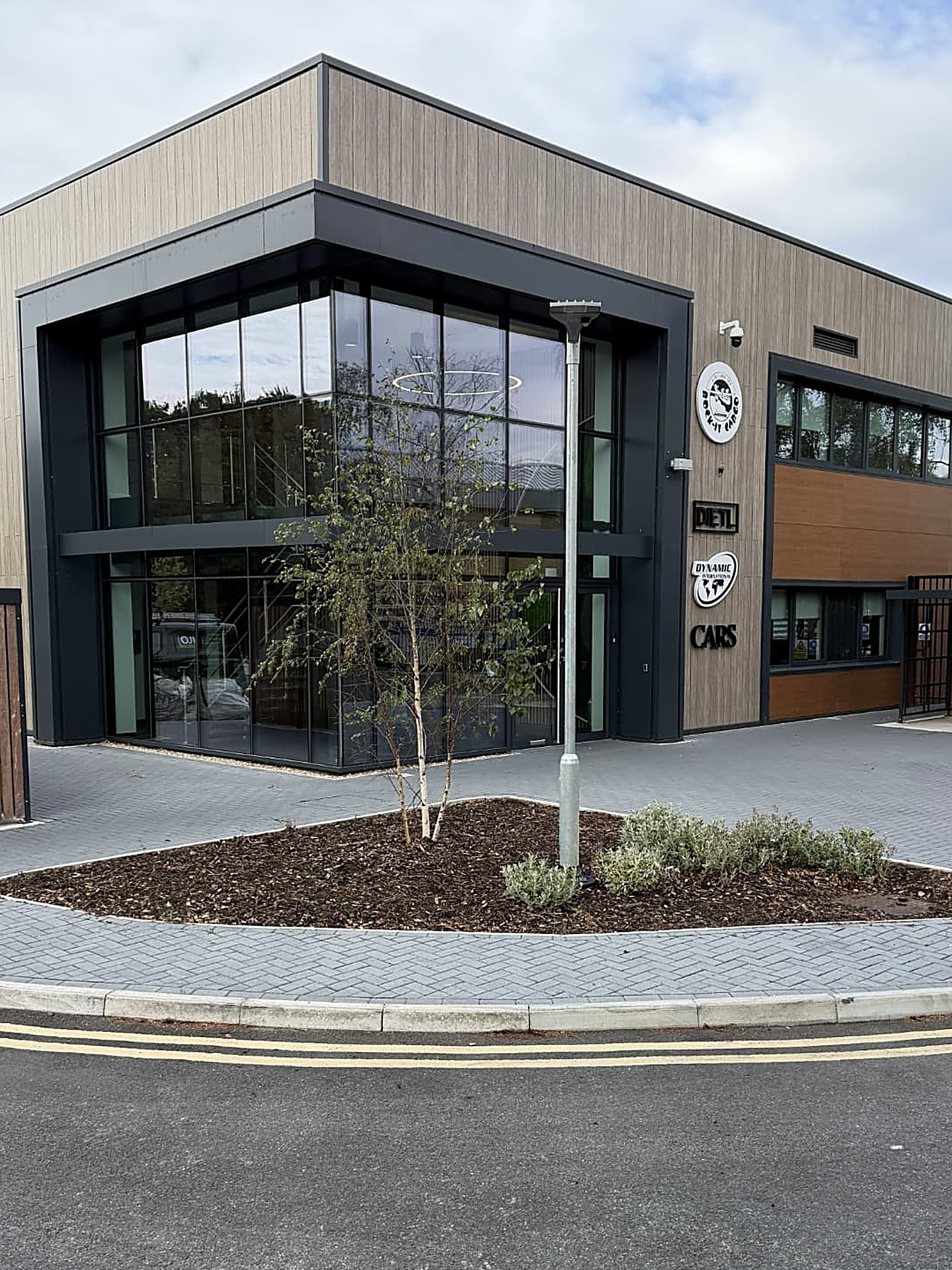 A paved footpath and mulched planting bed in front of a modern glass-fronted office building